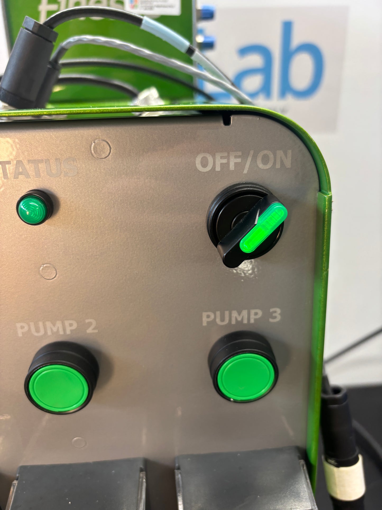 Control panel with green buttons and labels on a machine, with 'Qlab' branding in the background.