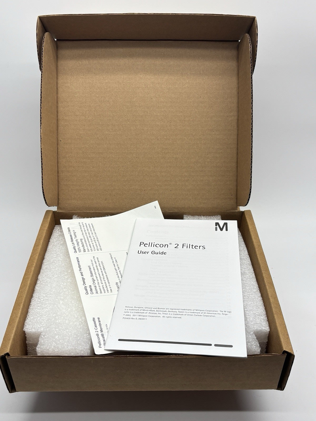 Open cardboard box with Pellicon 2 Filters user guide and documents on a white background